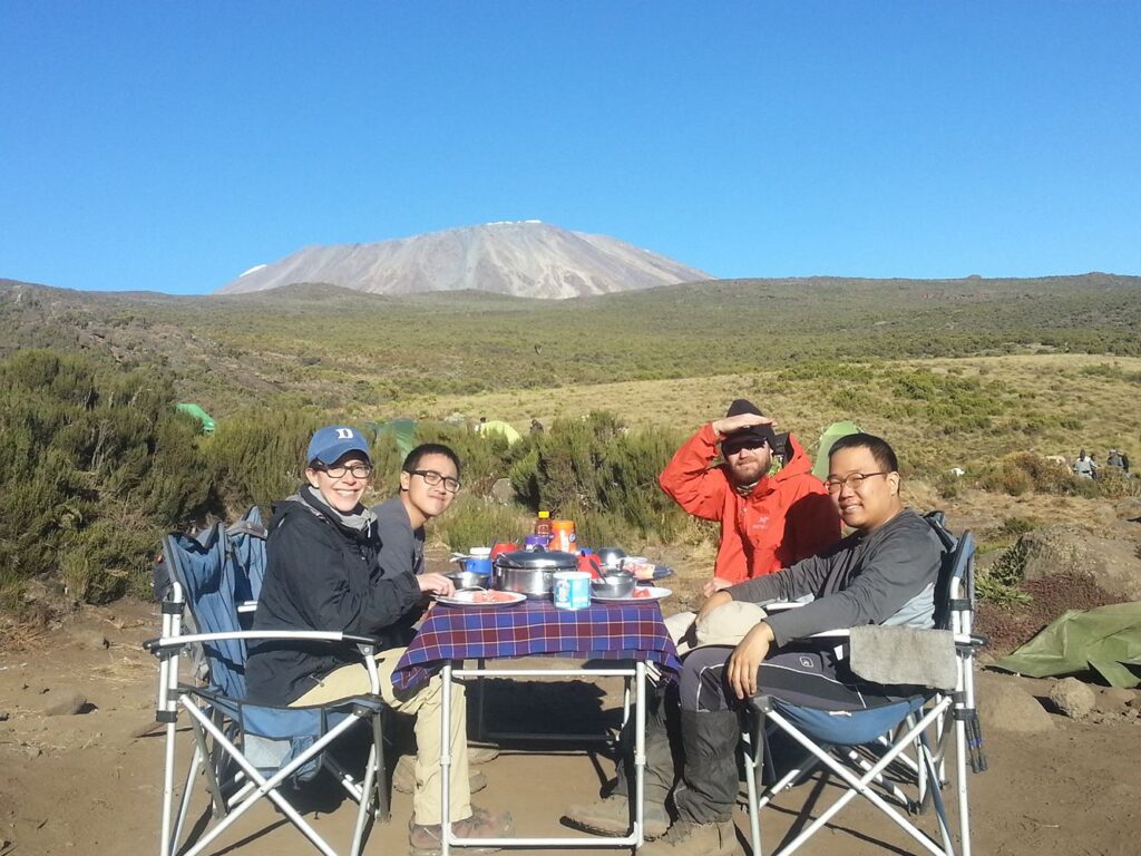 four trekkers having a meal in front of a mountain